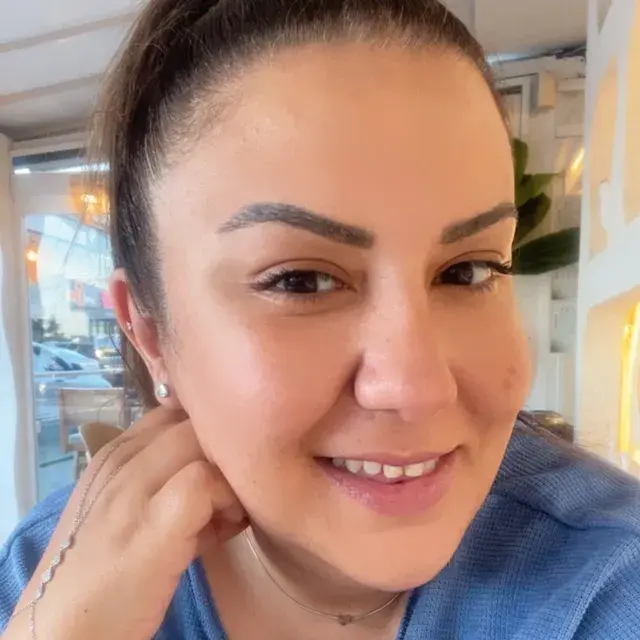 Merve Doğan; mavi örgü kazakla, gün ışığı alan bir kafede gülümserken