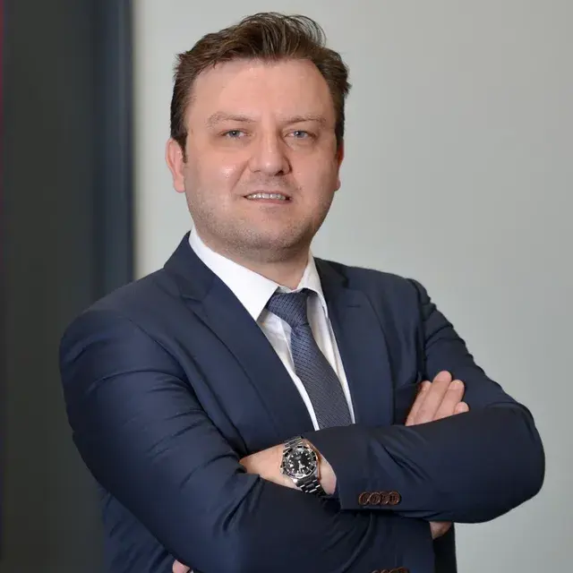 Abdullah Doğan; lacivert takım elbiseyle, kolları bağlı, hafif gülümseyen bir portre