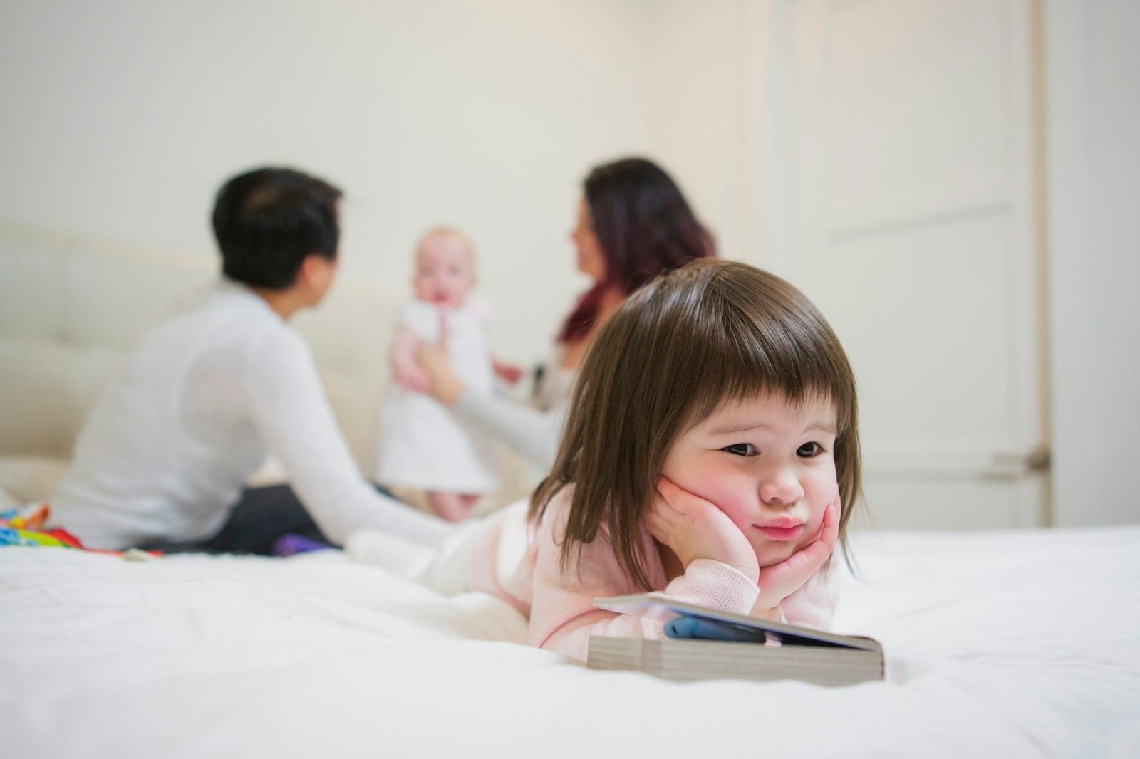 Fed up girl toddler lying on bed in front of female parents and baby girl